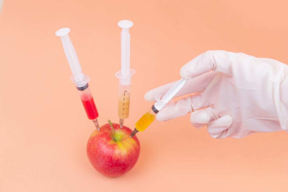 An apple being injected with a syringe of chemicals
